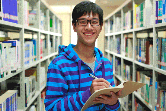澳大利亚国际学生男性站在图书馆里用记事本写作